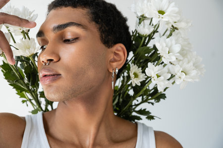 portrait of african american man with silver piercing posing near white fresh flowers isolated on greyの写真素材