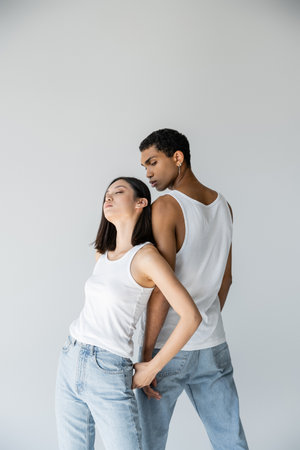 sensual asian woman with closed eyes leaning on african american man in white tank top and jeans...