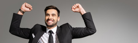 successful and overjoyed businessman showing triumph gesture isolated on grey, bannerの写真素材