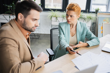 worried businesswoman pointing at charts while talking to manager in officeの写真素材