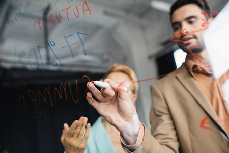blurred businessman with felt pen writing on clipboard near woman pointing with hand in officeの写真素材