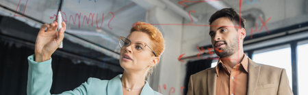 businesswoman with felt pen writing on glass board near bearded colleague in office, banner