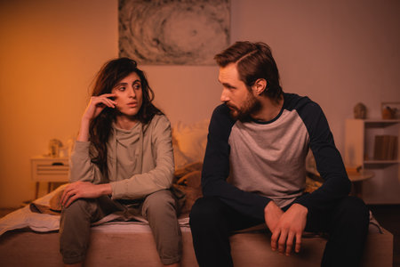 Dissatisfied woman talking to bearded boyfriend on bed in eveningの写真素材