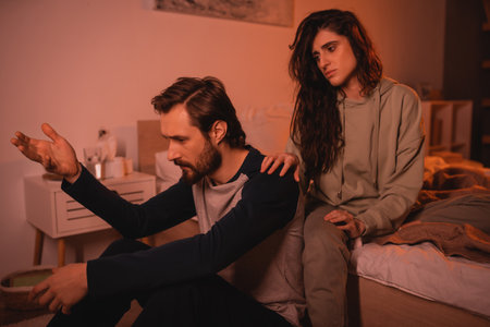 Brunette woman calming down upset boyfriend talking in bedroom in eveningの写真素材