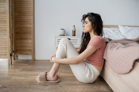 Side view of displeased woman in pajama sitting on floor in bedroomの写真素材
