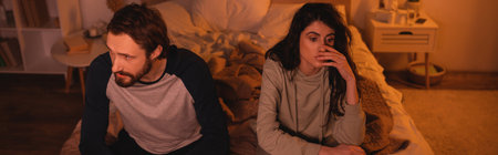 Sad woman sitting near boyfriend on bed at night, bannerの写真素材