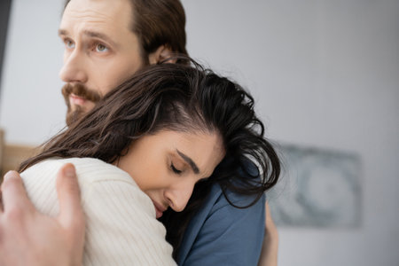 Caring man hugging and consoling sad brunette girlfriend at homeの写真素材