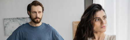 Bearded man looking at offended blurred girlfriend at home, bannerの写真素材