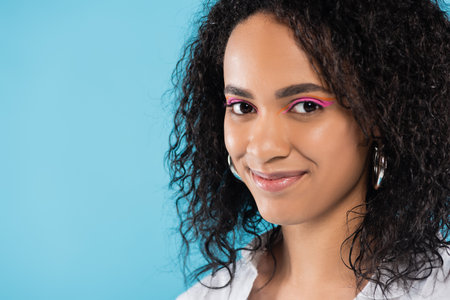 portrait of brunette african american woman with makeup and perfect skin looking at camera isolated on blueの写真素材