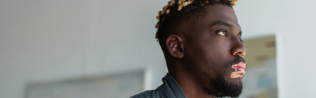Young african american man with vitiligo looking away at home, banner