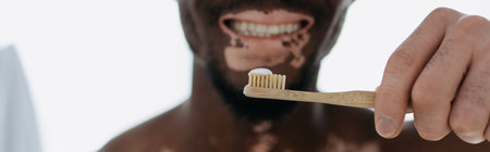 Cropped view of smiling african american man with vitiligo holding toothbrush at home, bannerの写真素材