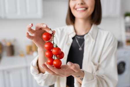 Cropped view of blurred smiling woman holding cherry tomatoes in kitchenの写真素材
