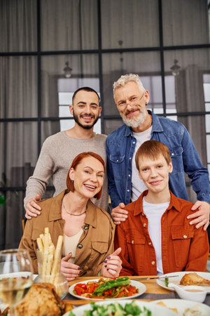 young gay couple with happy parents looking at camera near delicious supper at homeの写真素材