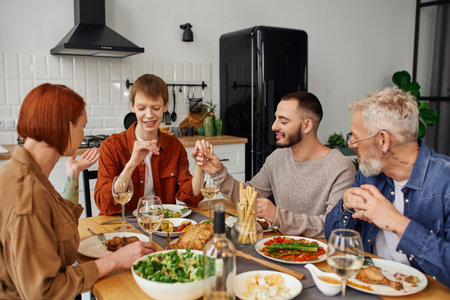 bearded gay man holding hand of redhead boyfriend and showing wedding ring to parents during supper in kitchenの写真素材