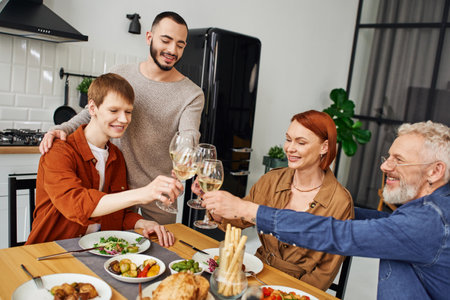 happy gay man clinking wine glasses with boyfriend and parents near delicious supper in kitchen