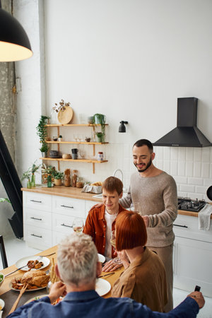 joyful man toasting with wine during delicious supper with parents and boyfriend in kitchenの写真素材