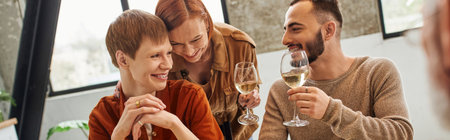 bearded gay man toasting with wine near happy boyfriend and redhead woman in kitchen, bannerの写真素材