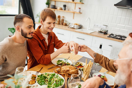 pleased gay man showing wedding ring during family dinner with boyfriend and parents in kitchenの写真素材