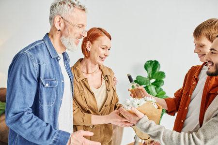 cheerful gay couple giving flowers and bottle of wine to cheerful parents meeting them at home