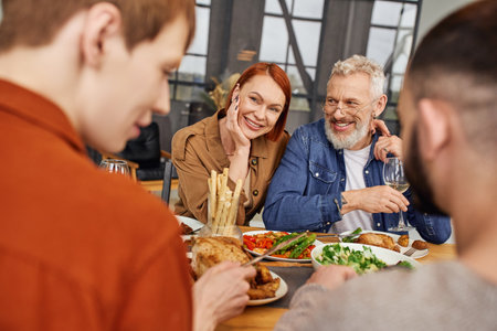 happy couple looking at son with gay partner having delicious supper in living room