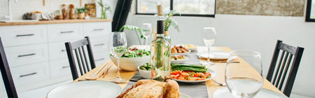 bottle and wine glasses near fried chicken and vegetables served on table in modern kitchen, banner