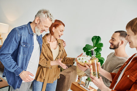 young gay couple visiting happy parents at home while holding flowers and bottle of wineの写真素材