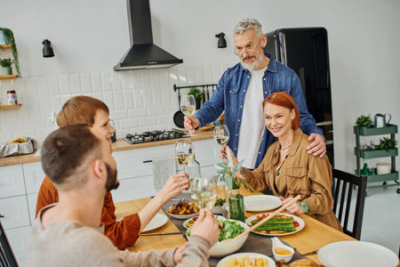 bearded man looking at young gay couple and toasting with wine glass near delicious supper in...