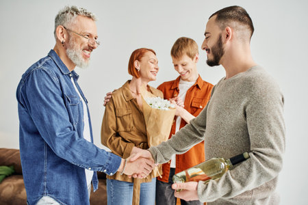 pleased father shaking hands with gay man near mother and son with flowers at homeの写真素材