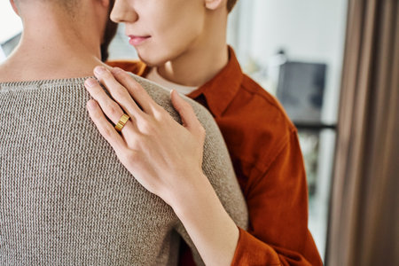 partial view of gay man in wedding ring embracing partner at homeの写真素材