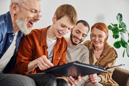 young gay man looking at photo album near bearded boyfriend and cheerful parentsの写真素材