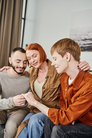 happy redhead woman hugging gay man and son looking at wedding ring at homeの写真素材