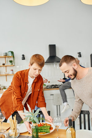 redhead gay man serving grilled asparagus near boyfriend in modern kitchenの写真素材