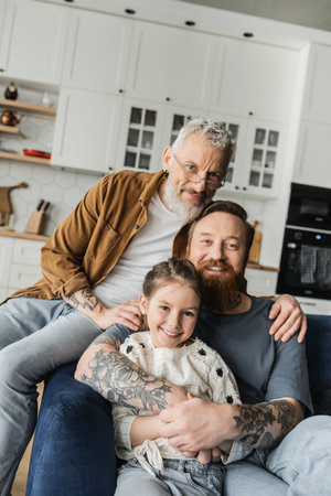 Same sex parents smiling and hugging adopted daughter at home