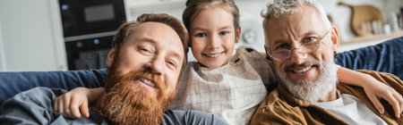 Carefree preteen girl hugging bearded gay fathers on couch at home, banner