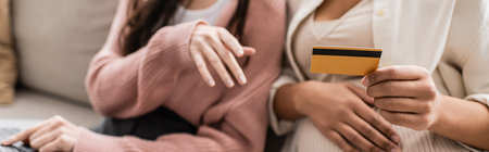 partial view of pregnant multiracial woman holding credit card near lesbian partner, banner