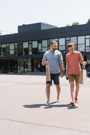 bearded father and teenage son walking from mall with shopping bags