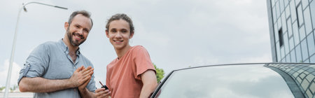 happy father and teenage son standing together near modern car, banner