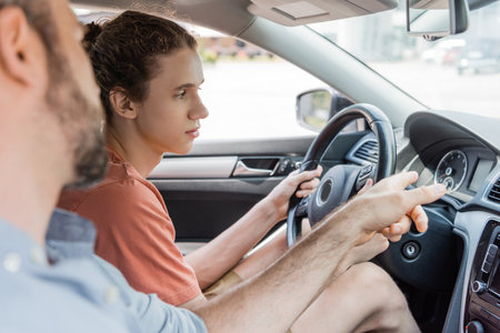 bearded father pointing at speedometer while teaching teenage son how to drive carの写真素材