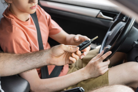 cropped view of father giving car key to teenage son sitting next to steering wheelの写真素材