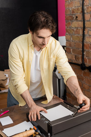 tattooed man using paper trimmer machine in modern print center