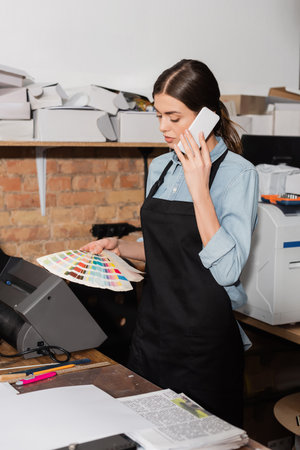 typographer in apron looking at color samples while having phone call in print center