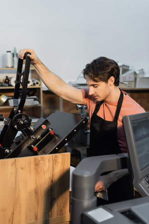 man in apron using professional print plotter while working in print center