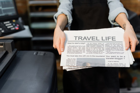 partial view of typographer with tattoo on hand holding freshly printed newspapersの写真素材