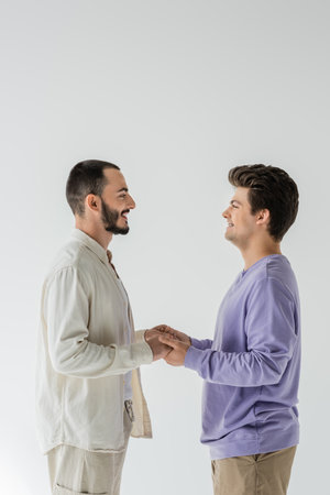 Side view of smiling homosexual couple in casual clothes looking at each other and holding hands...