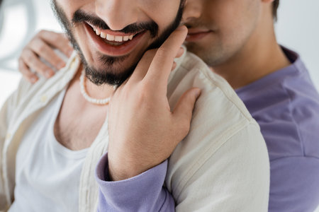 Cropped view of blurred homosexual man in casual clothes hugging and touching beard of carefree partner in casual clothes on grey backgroundの写真素材