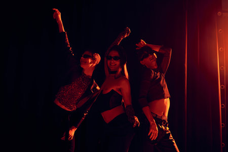 Smiling group of homosexual friends in stylish clothes and sunglasses posing during party and lgbt pride month celebration on black background with red lightingの写真素材