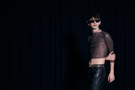 Trendy young gay man in sunglasses, sparking top and leather pants posing while celebrating lgbt...