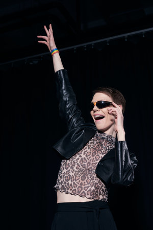 Carefree nonbinary person in stylish sunglasses, leather jacket and blouse with animal print...