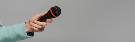Cropped view of hand of event host in green jacket holding black wireless microphone during party isolated on grey with copy space, bannerの写真素材