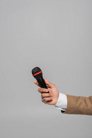 Cropped view of young event host in blue jacket and white shirt holding wireless microphone while standing isolated on grey with copy spaceの写真素材